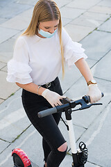 Image showing Trendy fashinable girl wearing corona virus protective face mask and rubber gloves while using rental electric scooters in city environment. Eco-friendly city transport in Ljubljana, Slovenia