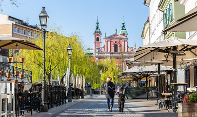 Image showing Rear view of unrecognizable woman walking a dog in empty old medieval Ljubljana city center during corona virus pandemic. Empty bars and restaurants. Almost no people outside on streets