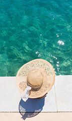 Image showing Woman wearing big summer sun hat relaxing on pier by clear turquoise sea.