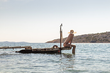 Image showing View of unrecognizable woman wearing big summer sun hat tanning topless and relaxing on old wooden pier in remote calm cove of Adriatic sea, Croatia