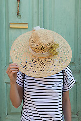 Image showing Unrecognizable female tourist woman wearing big straw standing in front of vinatage turquoise wooden door at old Mediterranean town.