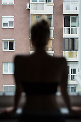 Image showing Home quarantine and social distancing during covid pandemic. Silhouette of lonley caucasian woman standing by window, anxiously looking out. Coronavirus infection, pandemics, disease outbreaks