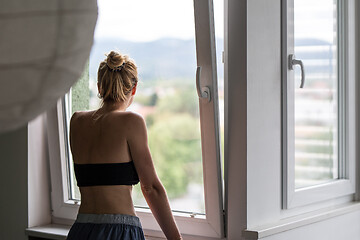 Image showing Home quarantine and social distancing during covid pandemic. Silhouette of lonley caucasian woman standing by window, anxiously looking out. Coronavirus infection, pandemics, disease outbreaks