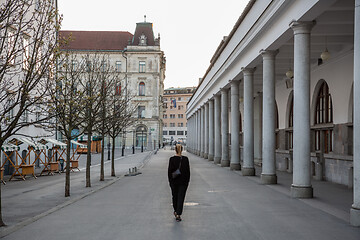 Image showing Rear view of unrecognizable woman walking in empty old medieval Ljubljana city center during corona virus pandemic. Almost no people outside on streets