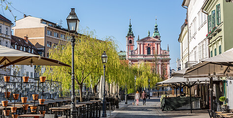 Image showing Rear view of unrecognizable woman walking a dog in empty old medieval Ljubljana city center during corona virus pandemic. Empty bars and restaurants. Almost no people outside on streets