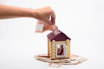 Image showing Hand shoves a five thousandth bill into the roof of a house