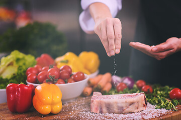 Image showing Chef putting salt on juicy slice of raw steak