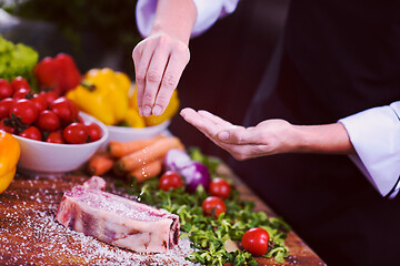 Image showing Chef putting salt on juicy slice of raw steak