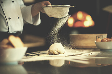 Image showing chef sprinkling flour over fresh pizza dough