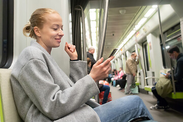 Image showing Portrait of lovely girl typing message on mobile phone in almost empty public subway train. Staying at home and social distancing recomented due to corona virus pandemic outbreak