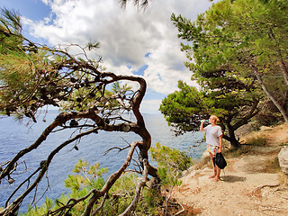 Image showing Young active feamle tourist taking a break, drinking water, wearing small backpack while walking on coastal path among pine trees looking for remote cove to swim alone in peace on seaside in Croatia