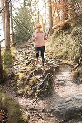 Image showing Active sporty woman listening to the music while running in autumn fall forest. Female runner training outdoor. Healthy lifestyle image of young caucasian woman jogging outside