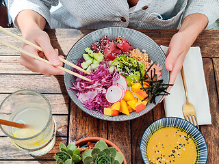 Image showing Woman eating tasty colorful healthy natural organic vegetarian Hawaiian poke bowl using asian chopsticks on rustic wooden table. Healthy natural organic eating concept