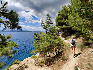 Image showing Young active feamle tourist wearing small backpack walking on coastal path among pine trees looking for remote cove to swim alone in peace on seaside in Croatia. Travel and adventure concept