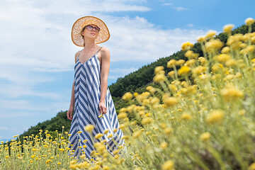 Image showing Young woman wearing striped summer dress and straw hat standing in super bloom of wildflowers, relaxing while enjoing beautiful nature of of Adriatic sea coastal nature of Croatia.