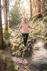 Image showing Active sporty woman running in autumn fall forest jumping over the roots on the path. Healthy lifestyle image of young active caucasian woman jogging outside in nature