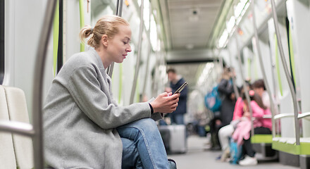 Image showing Portrait of lovely girl typing message on mobile phone in almost empty public subway train. Staying at home and social distancing recomented due to corona virus pandemic outbreak