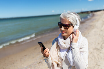 Image showing old woman in headphones with smartphone on beach