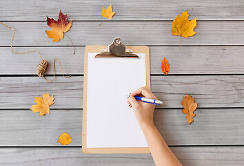 Image showing hand writing on white paper on clipboard in autumn