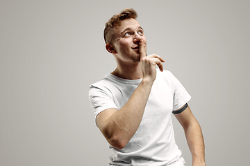 Image showing Keep silence. Handsome young man in white shirt looking at camera and holding finger on lips