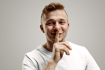 Image showing Keep silence. Handsome young man in white shirt looking at camera and holding finger on lips