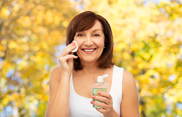 Image showing senior woman cleaning face by lotion on cotton pad