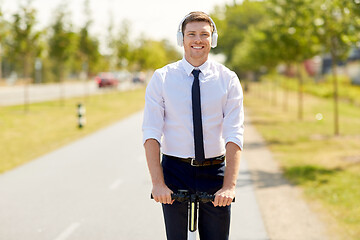 Image showing businessman with headphones riding scooter in city