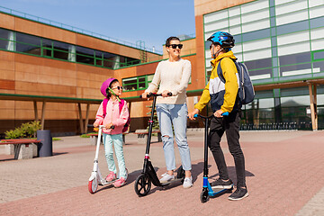 Image showing happy school children with mother riding scooters