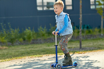 Image showing happy little boy riding scooter in city