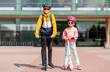 Image showing happy school children in helmets riding scooters