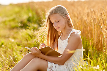 Image showing smiling girl writing to diary on cereal field