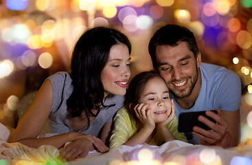 Image showing happy family with smartphone in bed at night