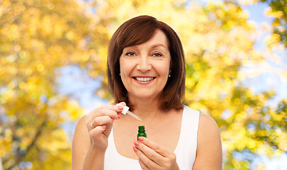 Image showing smiling senior woman with bottle of serum