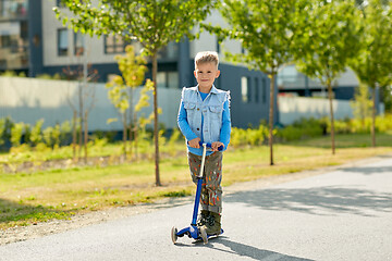 Image showing happy little boy riding scooter in city