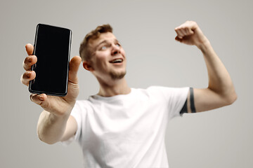 Image showing Young handsome man showing smartphone screen isolated on gray background in shock with a surprise face