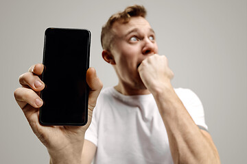 Image showing Young handsome man showing smartphone screen isolated on gray background in shock with a surprise face