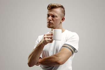 Image showing Taking a coffee break. Handsome young man holding coffee cup while standing against gray background