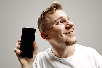 Image showing Young handsome man showing smartphone screen isolated on gray background in shock with a surprise face