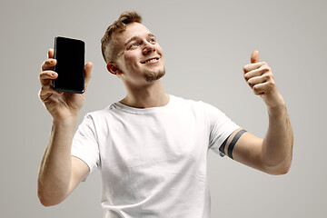 Image showing Young handsome man showing smartphone screen isolated on gray background in shock with a surprise face