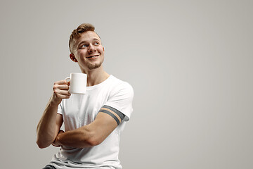 Image showing Taking a coffee break. Handsome young man holding coffee cup, smiling while standing against gray background