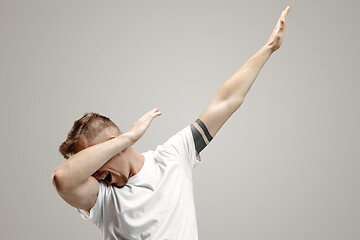 Image showing Young man makes the dab movement with his arms on a gray background.