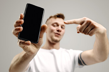 Image showing Young handsome man showing smartphone screen isolated on gray background in shock with a surprise face