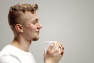 Image showing Taking a coffee break. Handsome young man holding coffee cup, smiling while standing against gray background