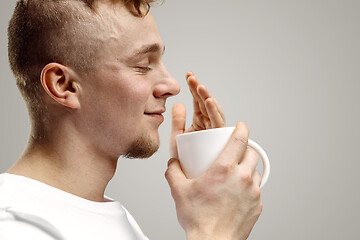 Image showing Taking a coffee break. Handsome young man holding coffee cup, smiling while standing against gray background