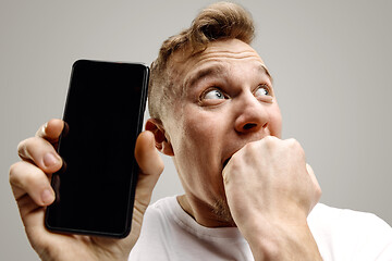 Image showing Young handsome man showing smartphone screen isolated on gray background in shock with a surprise face