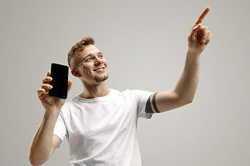 Image showing Young handsome man showing smartphone screen isolated on gray background in shock with a surprise face