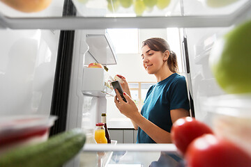 Image showing woman with smartphone makes list of food in fridge