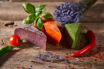 Image showing Three different cheeses on rough wooden planks: lavender, paprika and pesto cheeses