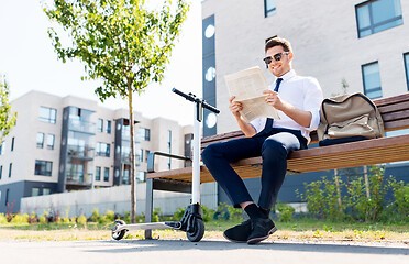 Image showing businessman with scooter reading newspaper in city