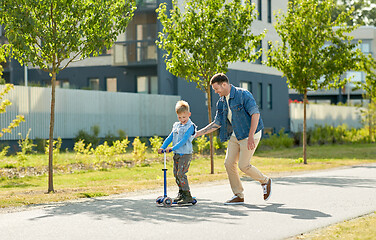 Image showing happy father and little son riding scooter in city